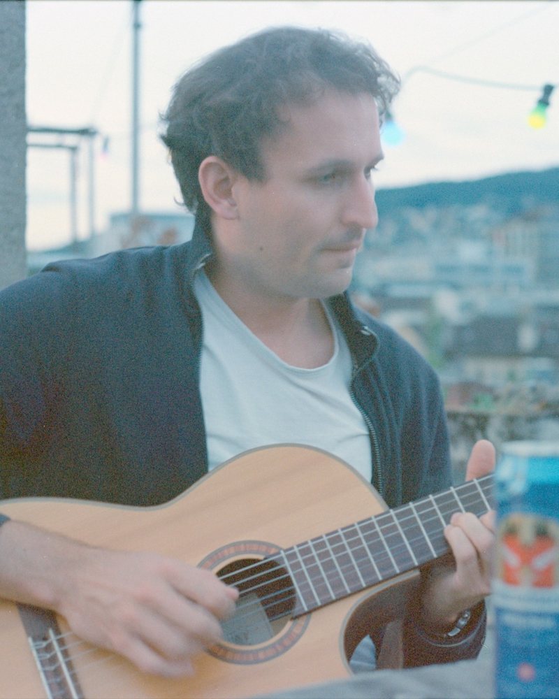 Hendrik Kolvenbach playing guitar on a rooftop in Zurich at dusk