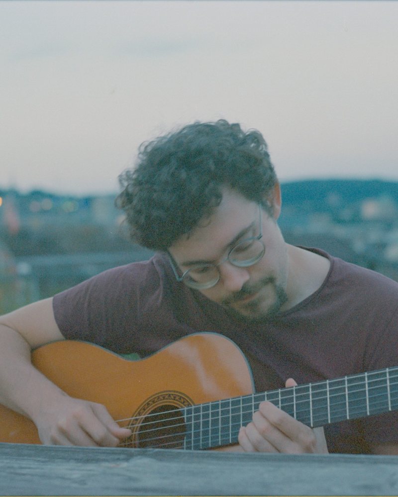 Miro Voellmy playing guitar on a rooftop in Zurich at dusk